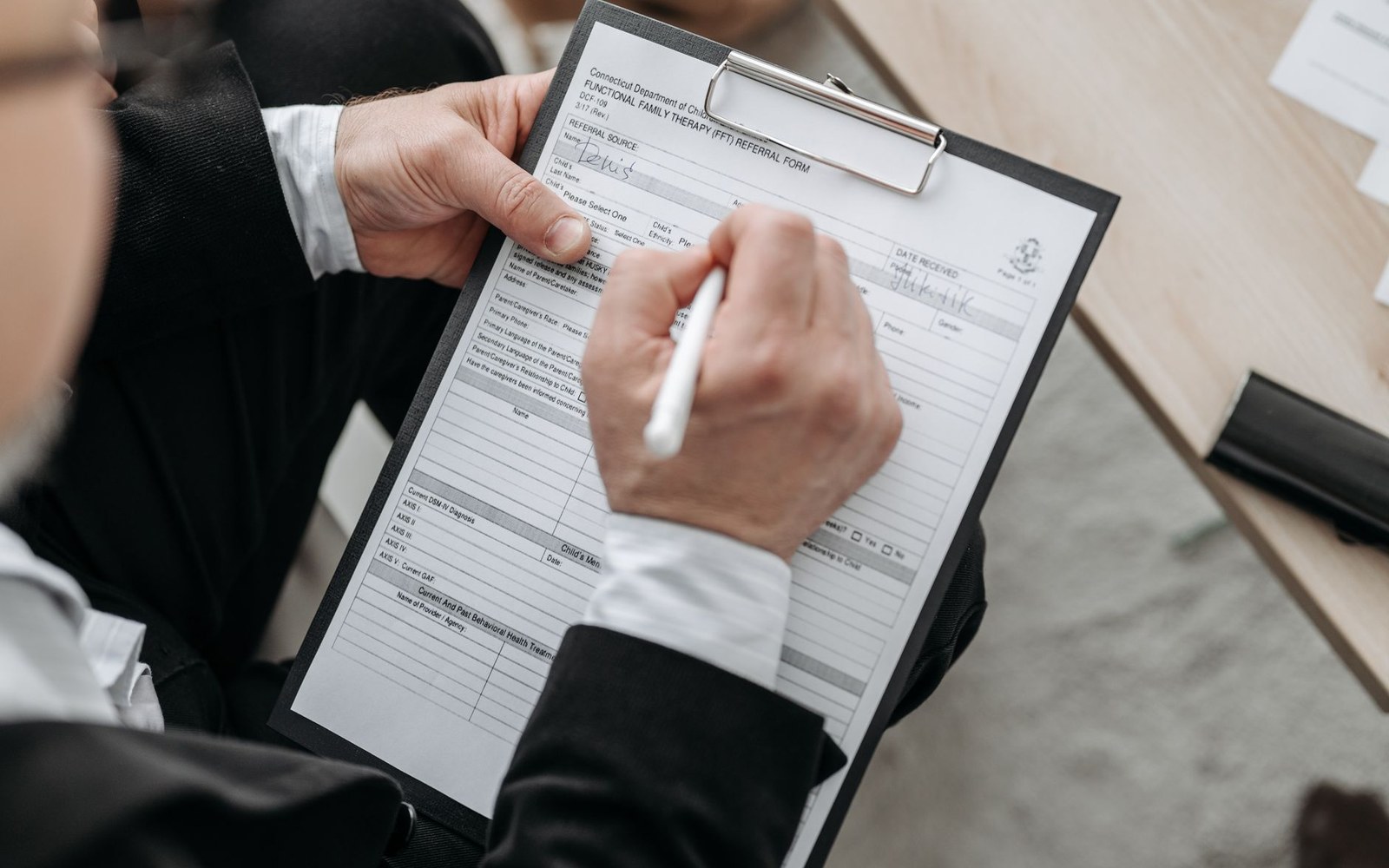 A hand fills out a family therapy referral form on a clipboard