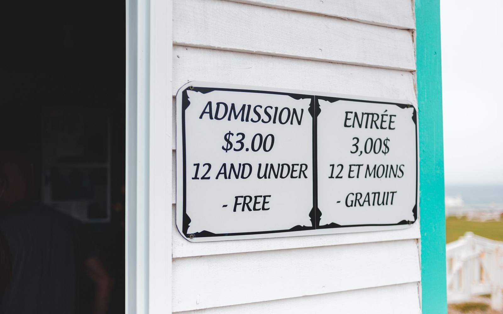 Bilingual sign on wooden siding lists admission as $3, free for children 12 and under