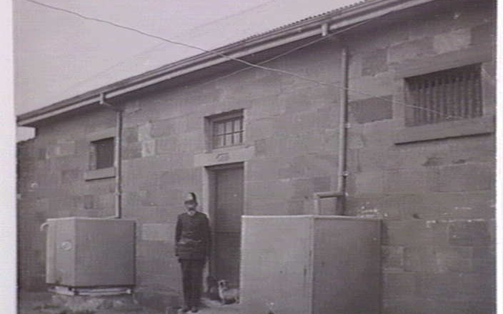 A uniformed officer stands with a dog beside the doorway of a stone gaol building