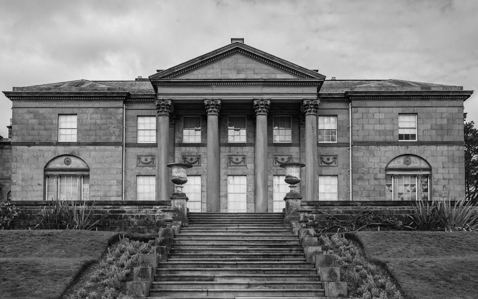 Neoclassical mansion facade with corinthian columns, urns, and a wide stone staircase